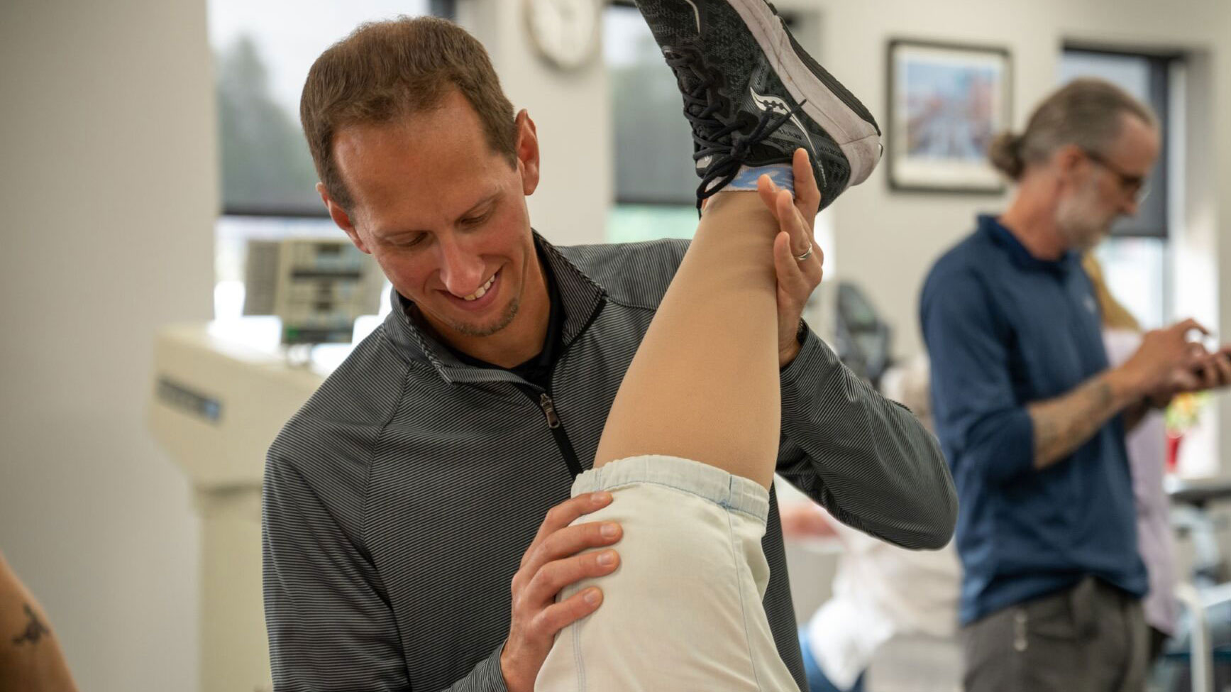 A Physical Therapist smiles as he stretches the leg of his patient.