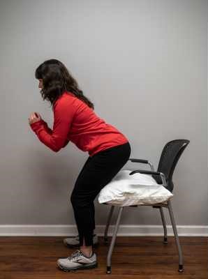 A Physical Therapist in a red sweatshirt demonstrates a squat. 