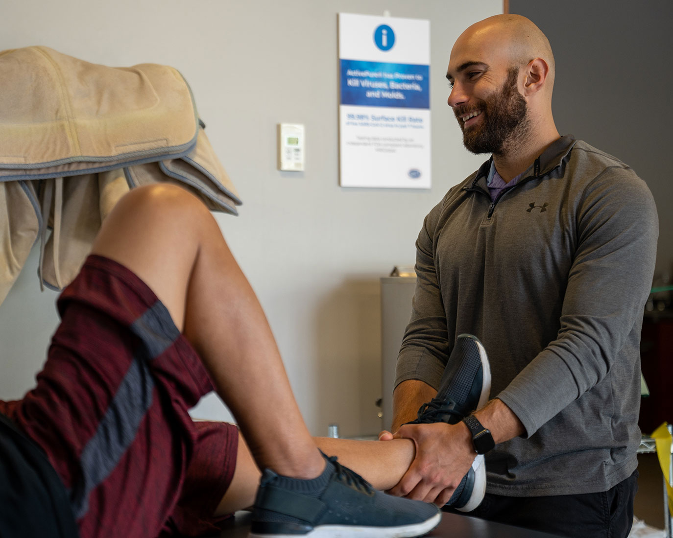 A Caucasian physical therapist smiles as he stretches the leg of his patient.