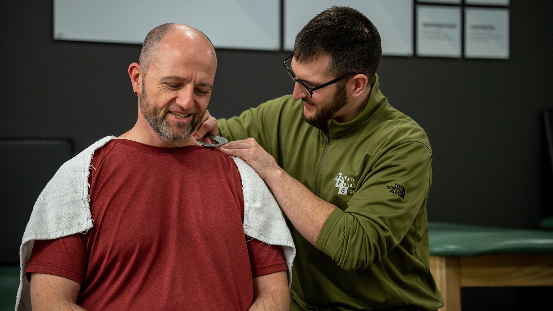 A physical therapist rubs the shoulders of his smiling patient.
