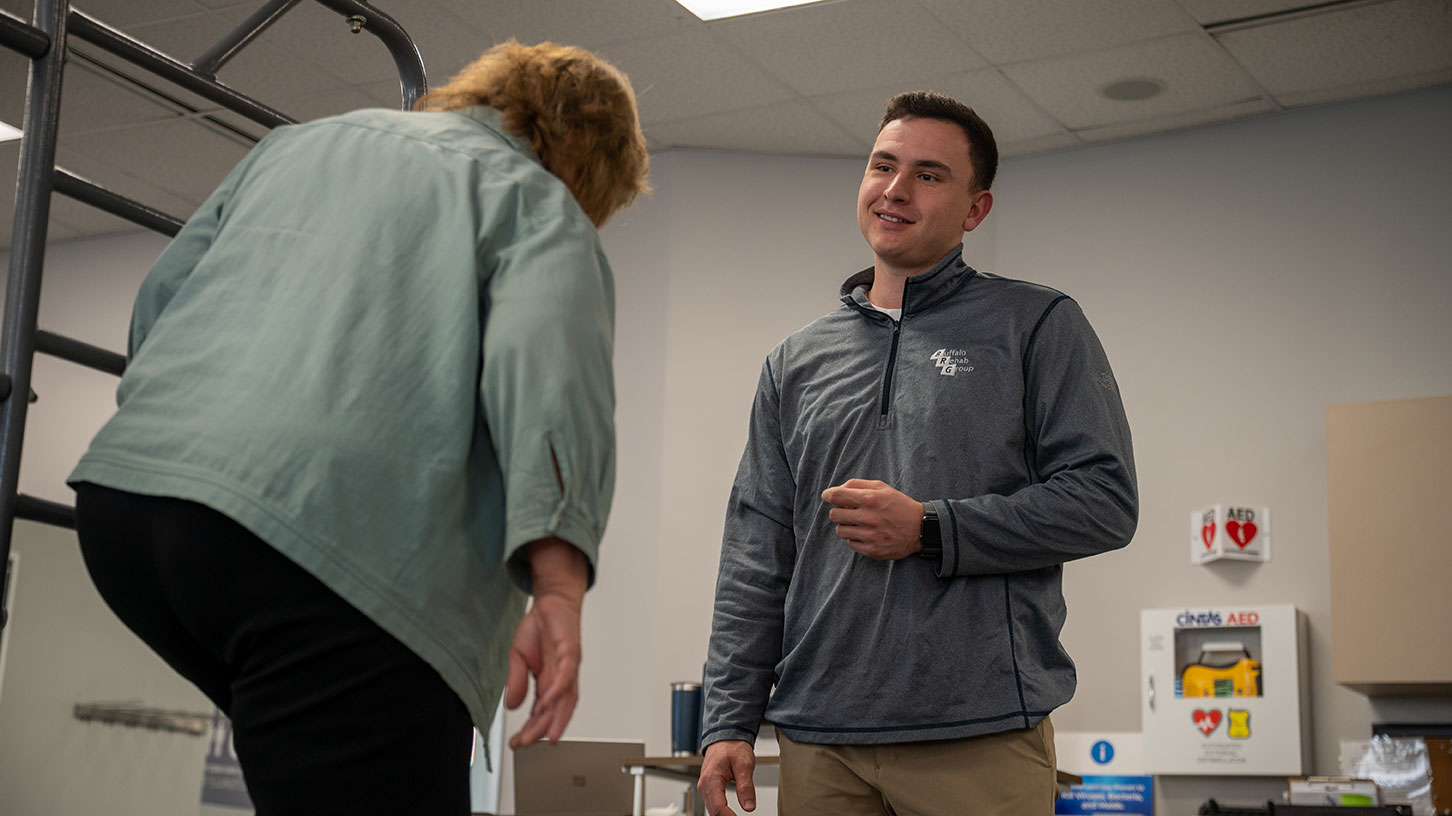 A physical therapist smiles as his patient walks toward him.