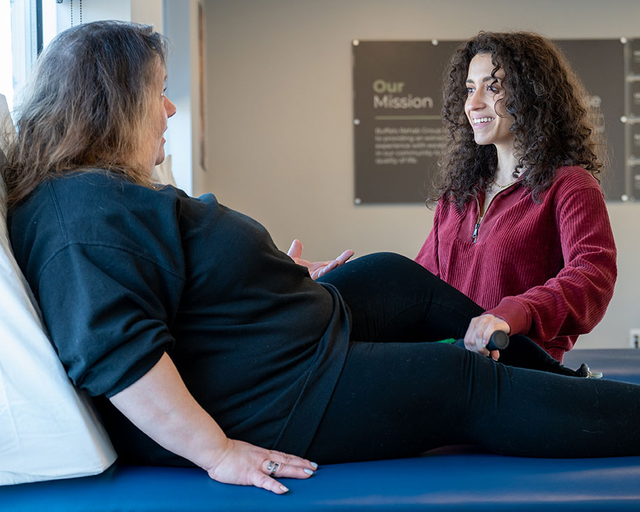 A physical therapist assistant smiles as she converses with her patient.