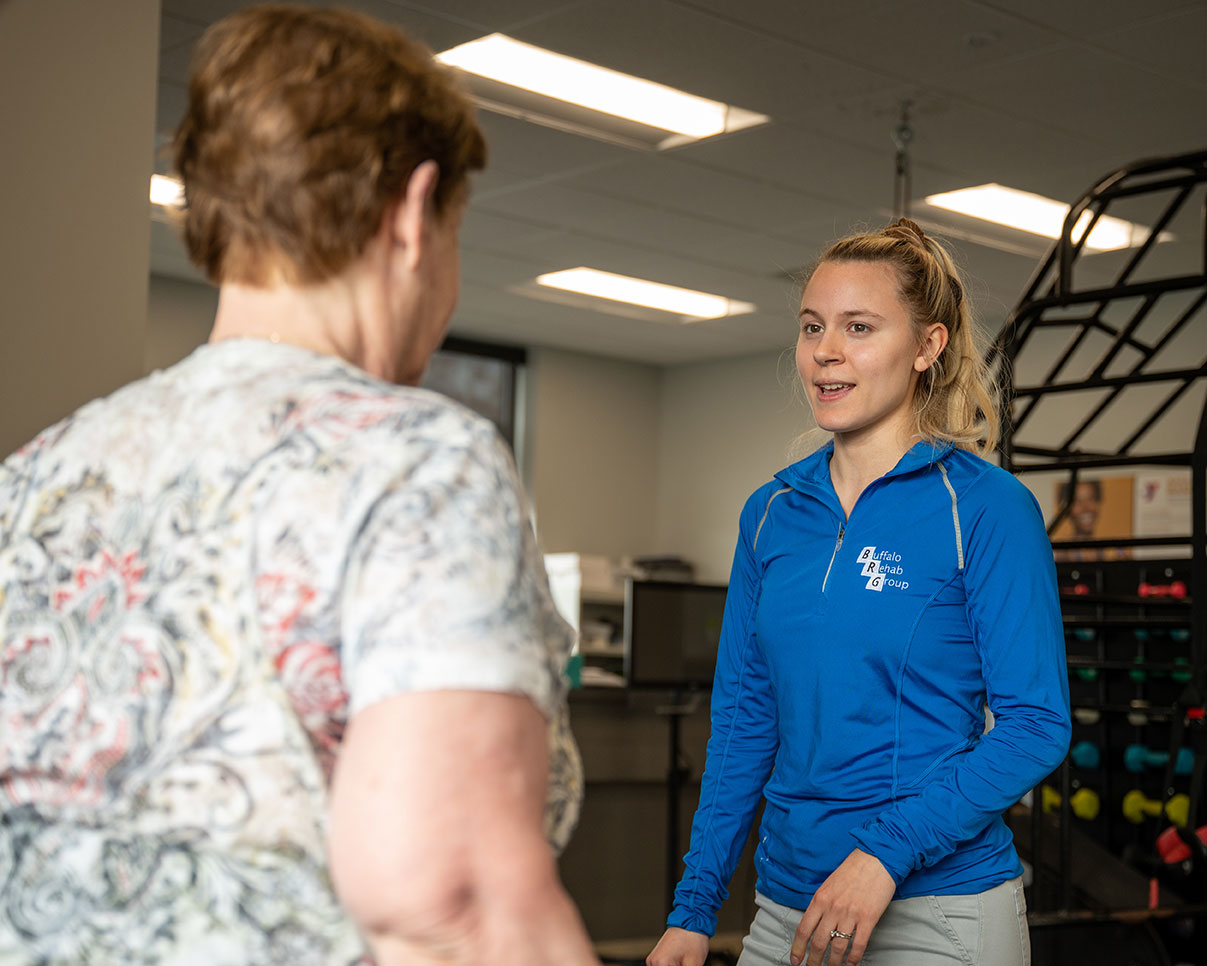 A physical therapist assistant smiles as her patient walks toward her.