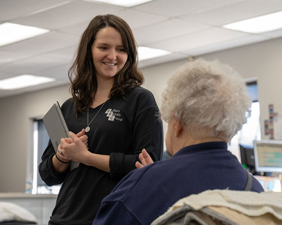 A physical therapist smiles as she converses with her patient.