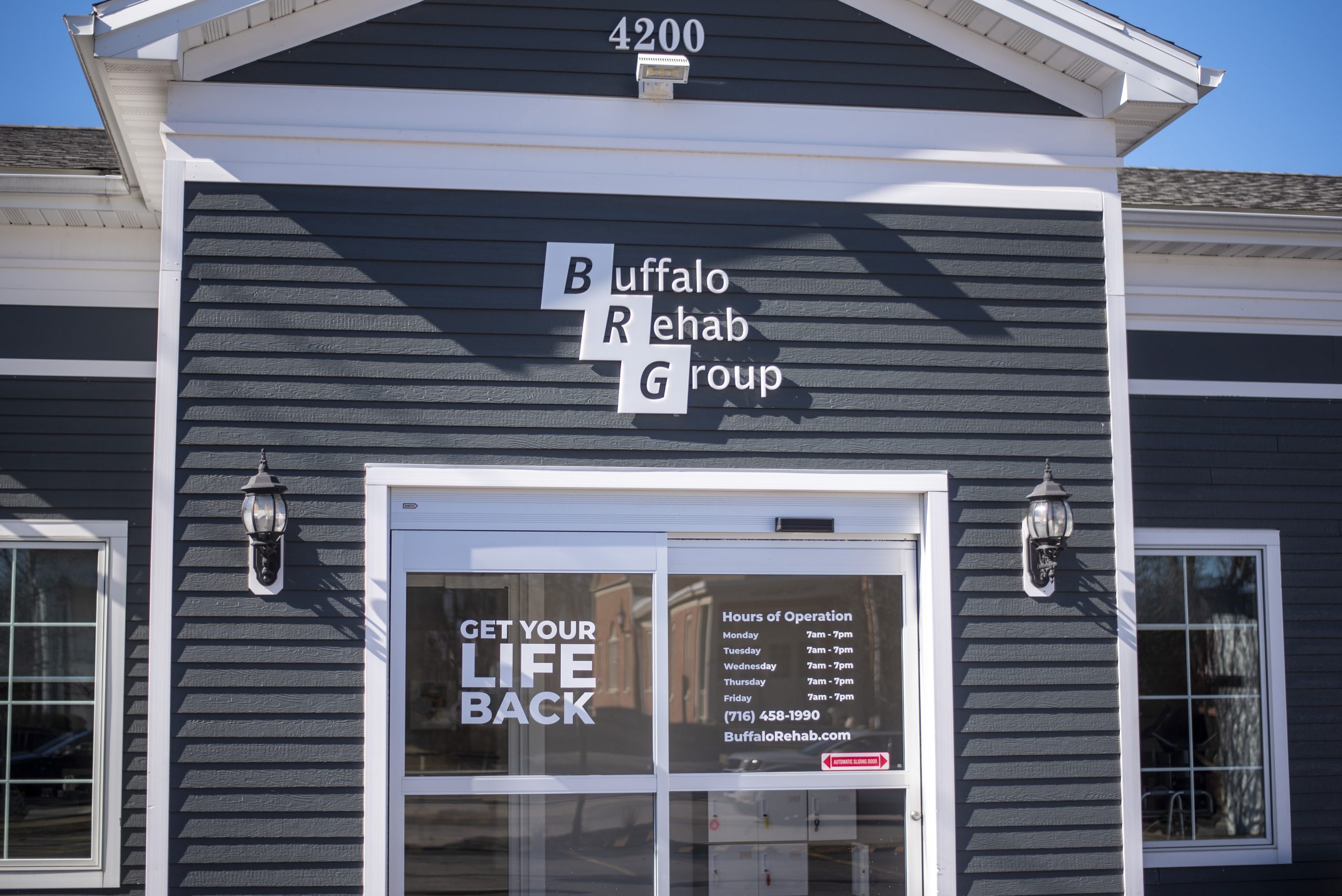 A dark gray physical therapy clinic sits in the sun with a "Buffalo Rehab Group" sign on the front.