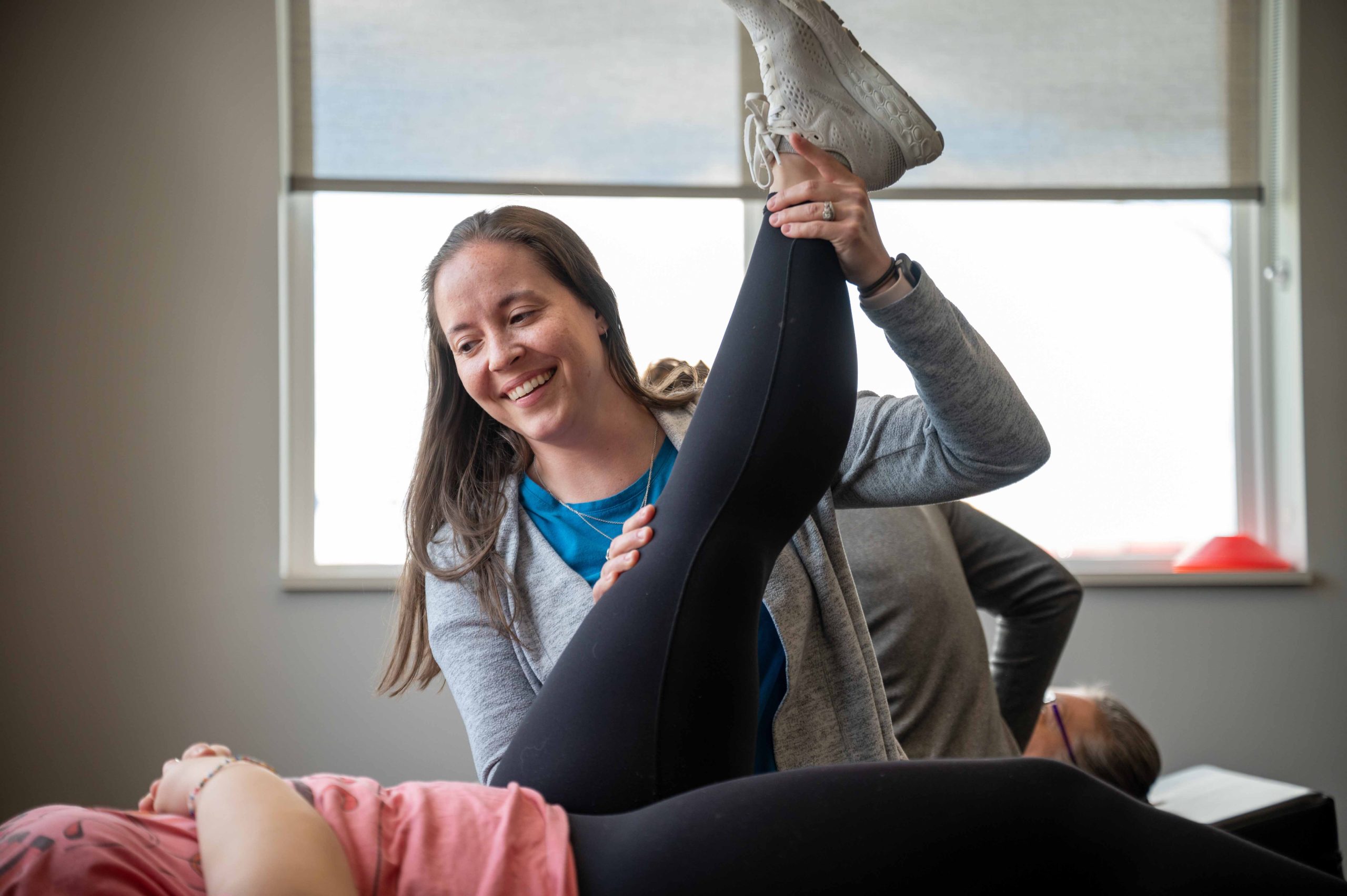 A physical therapist smiles as she stretches the leg of her patient.